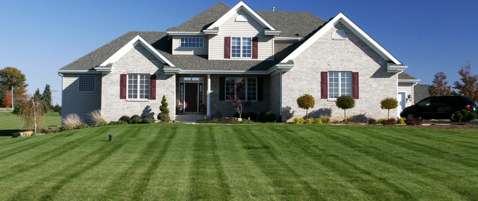 A large white brick home with a healthy lawn due to our services in Clayton, PA.